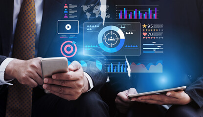 Two business professionals engage with mobile devices while analyzing digital data, showcasing a modern workspace with graphs and statistics that highlight teamwork and technology. Gantry