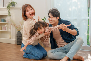 Happy Asian family playing together in living room, simulating flight. Shows family love and bonding.