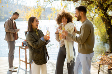 Friends celebrate by the lakeside, enjoying drinks and playfulness on a sunny day