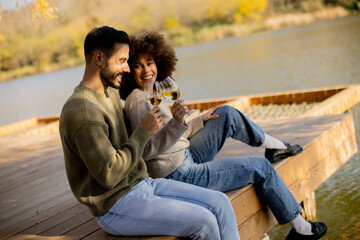 Joyful couple enjoying a sunny autumn afternoon by the lakeside with glasses of wine