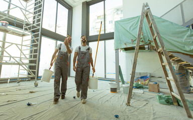 Fototapeta premium Workers with paint buckets walk in newly renovated room during daytime