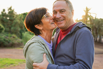 Obraz premium Happy senior couple having tender moment at city park during sunset time - Healthy elderly people and lifestyle concept