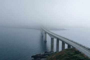 A long curved sea bridge stretches into dense fog over calm blue water, supported by tall concrete pylons, creating a surreal and moody coastal scene from above
