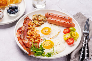 A classic breakfast plate featuring sunny-side-up eggs, crispy bacon, sausages, and fresh tomatoes