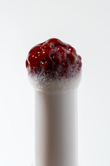 An elegant beauty product close-up: a clear applicator tip heavily coated in a glossy, deep red...