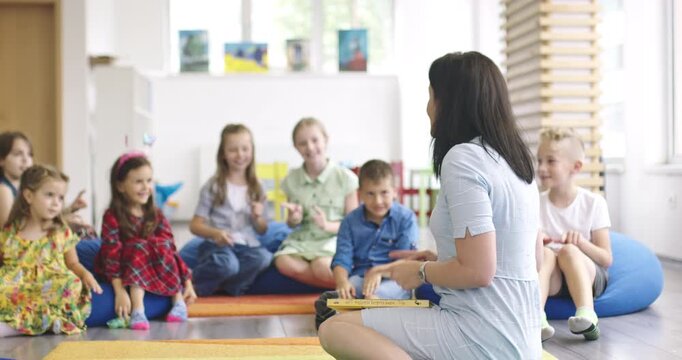 Energetic group of happy children running and playing a chasing game around their smiling teacher in a modern kindergarten classroom or sensory therapy room