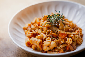 Pasta Fagioli soup in a white bowl with fresh rosemary, traditional italian comfort food