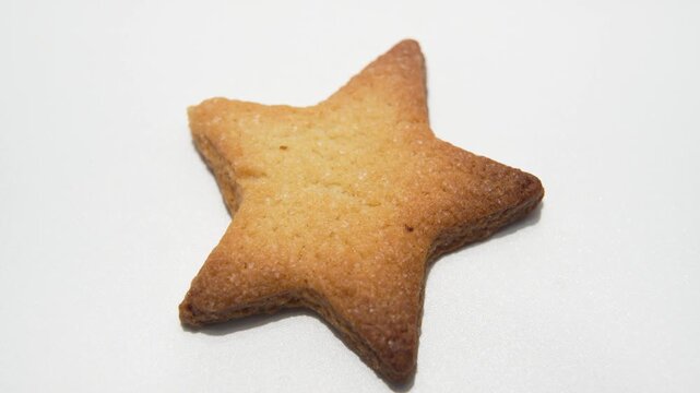 Star-Shaped Butter Cookie Top View. A golden star cookie slowly rotates, revealing crisp edges and even baking. The rotation highlights its symmetrical shape and fine sugar texture.