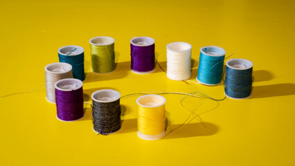 pequeñas bobinas de hilo de varios colores sobre fondo amarillo	
