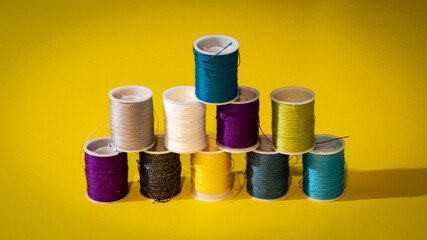 pequeñas bobinas de hilo de varios colores sobre fondo amarillo en forma de pirámide