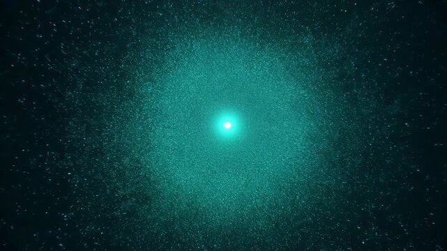 A vibrant cyan light expands in a dark, particle-filled space. This glowing energy creates an abstract, mesmerizing cosmic effect.