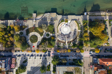 Top-down aerial view of Pogradec, Albania, featuring the lakeside amphitheatre, park areas, pedestrian squares, and Lake Ohrid shoreline.