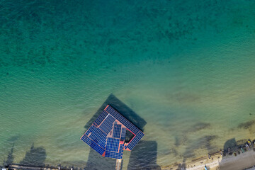op-down aerial view of a solar-powered pier extending into Lake Ohrid in Pogradec, Albania, surrounded by clear turquoise water and shoreline.