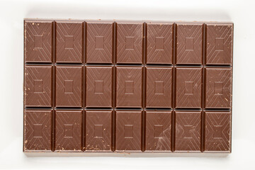 One bar of dark chocolate with a ceramic plate on a white background, close-up, top view.