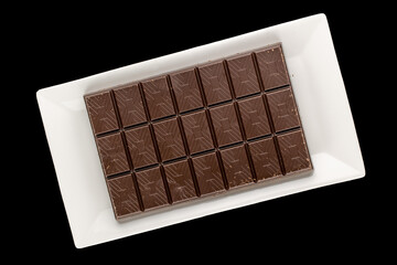 One bar of dark chocolate with a ceramic plate on a black background, close-up, top view.