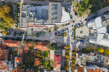 Top-down aerial view of a busy urban intersection in Pogradec, Albania, showing streets, parked cars, rooftops, and autumn trees.