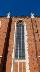 Wall and large window of a Gothic church and statues above. Gothic church built of brick against a blue sky background.