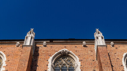 Wall and large window of a Gothic church and statues above. Gothic church built of brick against a blue sky background.