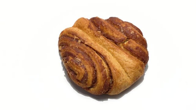 A cinnamon-style pastry rotates slowly, revealing layered dough and caramelized swirls. The rotation highlights its rich color and baked texture.