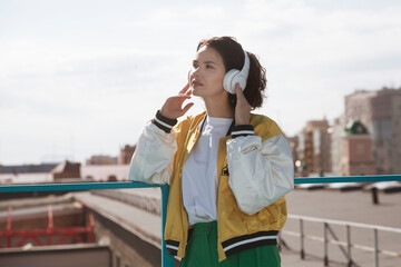 smiling middle aged woman with headphoneson  enjoying the view of the city from a high vantage point. Audio guide. Mindfulness and feel-good moments. Audio healing. 
