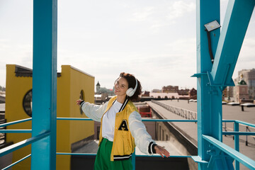 smiling middle aged woman with headphoneson  enjoying the view of the city from a high vantage point. Audio guide. Mindfulness and feel-good moments. Audio healing. 