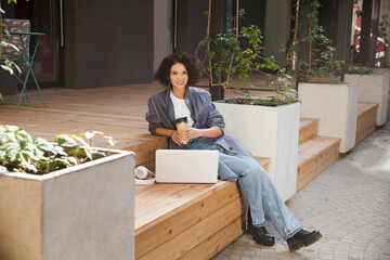  remote workers. Working from Anywhere.  middle aged woman    is working on a laptopon a bench on the street in a cafe. startup