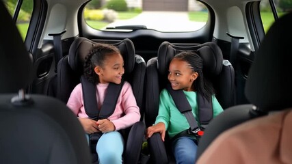 Two young girls safely seated in a car, buckled up and looking at each other, promoting car safety and family travel. Stock Video