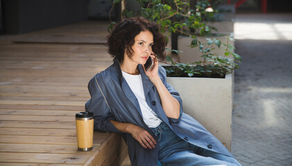  remote workers. Working from Anywhere.  middle aged woman    is working on a laptopon and talking on a mobile phone a bench on the street in a cafe. startup
