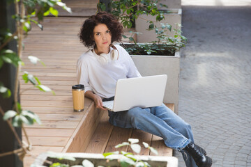  remote workers. Working from Anywhere.  middle aged woman    is working on a laptopon a bench on the street in a cafe. startup