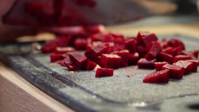 Close up of a person's hands slicing fresh raw beets with a sharp chef's knife on a dark cutting board in slow motion, highlighting healthy food preparation and home cooking in a cozy kitchen