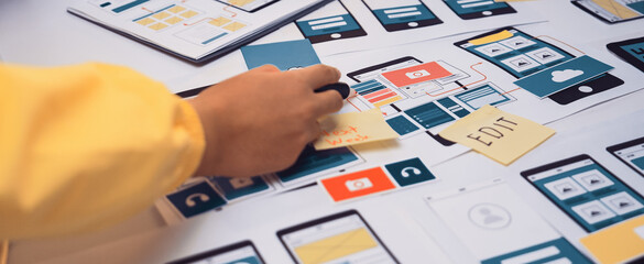 A close-up view of a hands-on mobile app design process featuring colorful sketches, notes, and prototypes laid out on a creative workspace table to showcase teamwork. SACTR