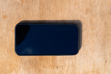 Smartphone with screen off placed horizontally on wooden surface in daylight