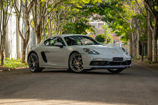 Grey Porsche 718 Cayman front three quarter view, german sports car parked on nature background