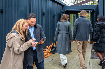 Business people discussing with digital tablet outside as coworkers entering to work in a modern office building constructed from shipping containers. Sustainable and eco friendly architecture concept