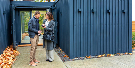Banner of architect explaining design concepts of modern modular house built from repurposed shipping containers in mobile phone to a satisfied client, with autumn leaves on the ground