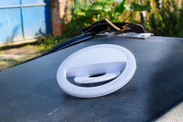 White LED ring light with clip placed on car hood outdoors