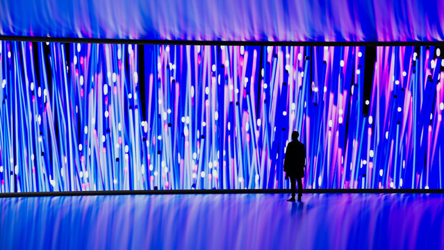 Man looks at digital screen with vibrant patterns in dark room