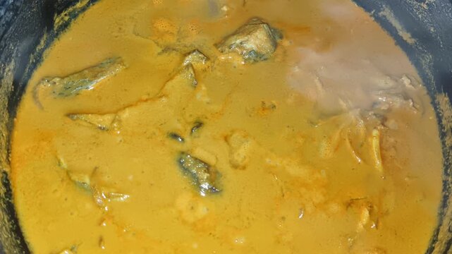 Traditional spicey south indian or kerala malabar style yellow fish curry with green mango and coconut milk. Homemade delicious stewed asian local seafood meat dish in cooking plate closeup top view.