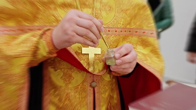 Priest Performing Sacred Hand Gesture, Clergyman Conducting Solemn Ceremony With Gold Vestments And Religious Symbols, Priest Offers Blessing Using Gilded Cross And Sacred Oil In Church Setting