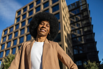 Person in brown blazer smiling against modern building