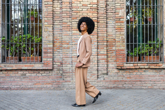 Person in brown blazer walking by a brick wall