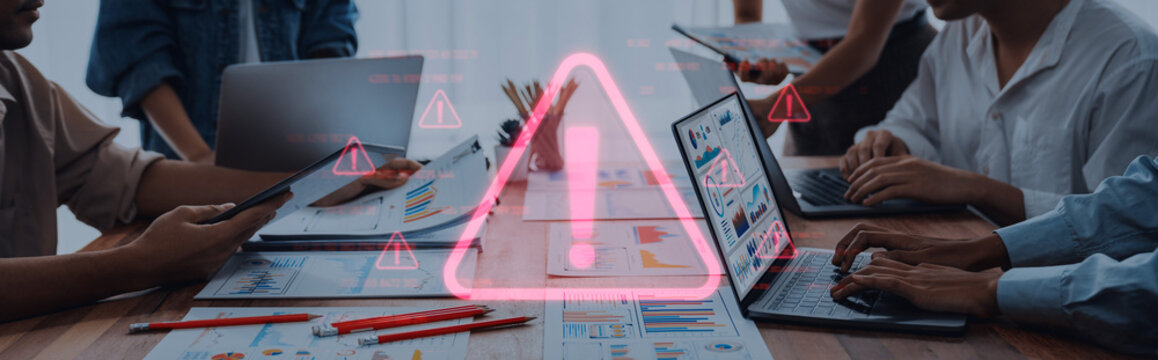 A group of professionals collaborates on a project in a modern office. They analyze data and discuss insights with alert symbols indicating challenges or warnings. Trope