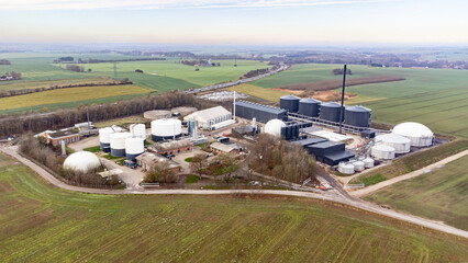 Drone aerial view of a biogas plant in rural Denmark, showing renewable energy infrastructure surrounded by farmland and countryside. © jespersoehof