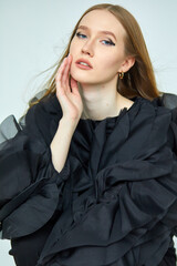 A beautiful woman in a stylish black dress, with long hair and flawless makeup, poses in front of the camera in a professional studio.