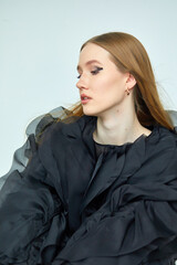 A beautiful woman in a stylish black dress, with long hair and flawless makeup, poses in front of the camera in a professional studio.