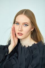 A beautiful woman in a stylish black dress, with long hair and flawless makeup, poses in front of the camera in a professional studio.