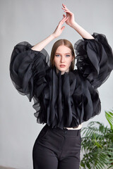 A beautiful woman in a stylish black dress, with long hair and flawless makeup, poses in front of the camera in a professional studio.
