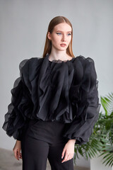 A beautiful woman in a stylish black dress, with long hair and flawless makeup, poses in front of the camera in a professional studio.