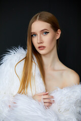 Portrait of a woman, taken in close-up. She is wearing a long white fur coat, and her hair is a chestnut shade.