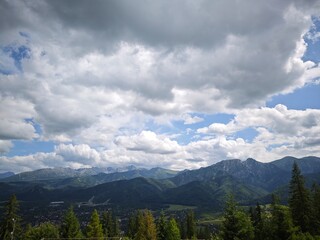 Massive mountains under cloudy blue sky above lush forest and distant town